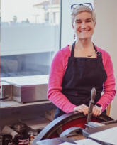 Woman in a black top and hot pink shrug standing behind an old printing press