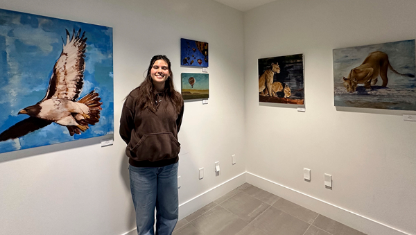April Hisey standing next to some of her art exhibit, Above the Horizon
