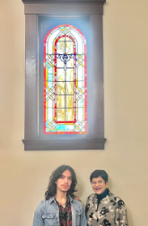 Alexis Alvarez Figueroa and Apara Nanda standing below a stained-glass window.