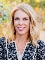 Meg Eppel Gudgeirsson standing in a vinyard next to ripe grapes on the vine