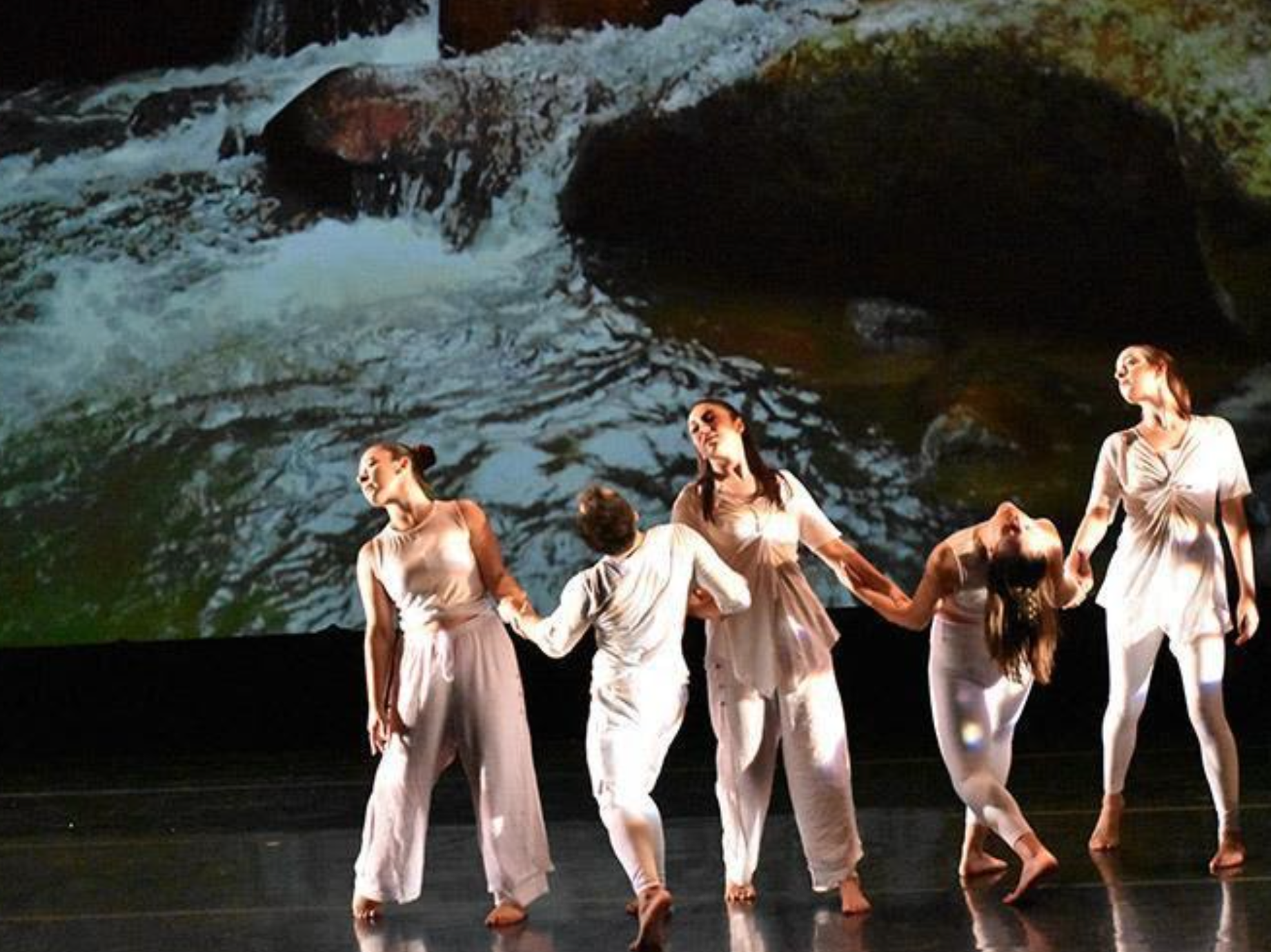 Group of dancers performing in front of a projected water image.