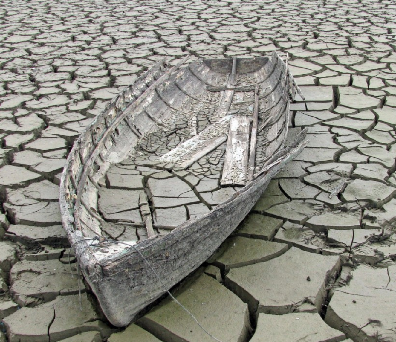 A boat stranded on a cracked, dry riverbed.