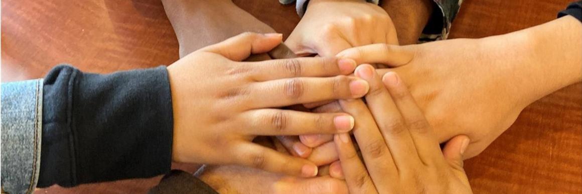 Four hands overlapping in a gesture of unity.