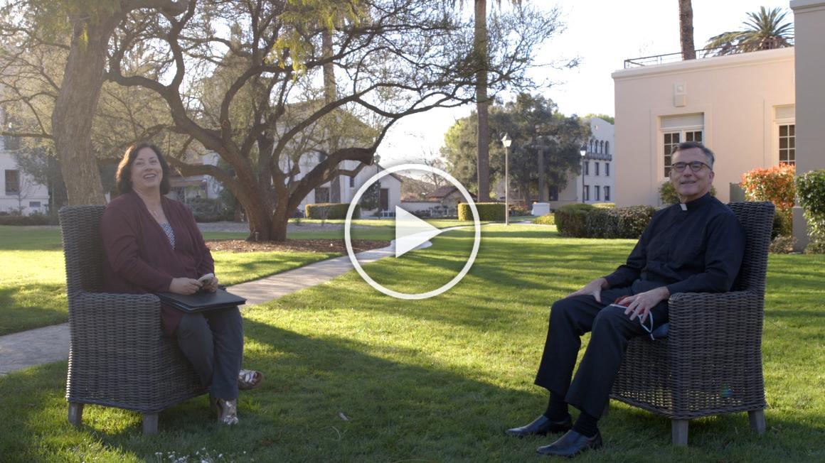 Two people sitting on chairs outdoors with a play button overlay.