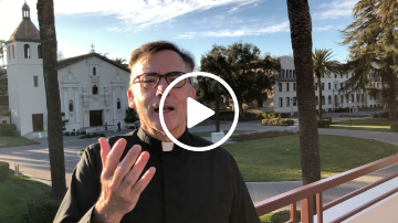 Person speaking outdoors with a play button overlay.