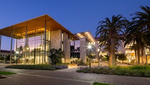 Exterior view of Sobrato Campus at dusk with lights and palm trees.