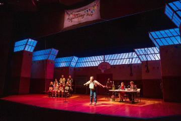 Contestant on stage in a spelling bee competition with judges and audience.
