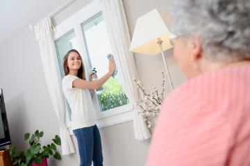 A woman helping an elderly person with daily activities in a home setting.