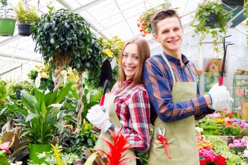 Two smiling people standing in a greenhouse with flowers.