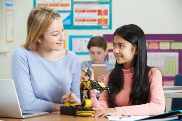 A teacher helping two students with a model of the human skeleton.