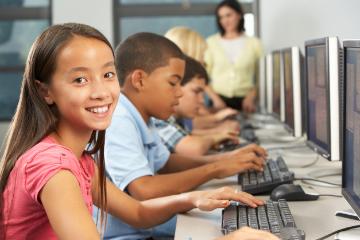 Middle school students working on computers in a classroom, with a teacher assisting.