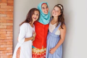 Three women smiling together, dressed in varied cultural attire.
