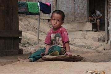 A child sitting on the ground with surroundings depicting poverty.