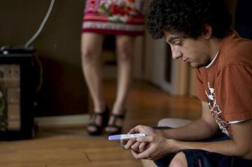 Teenager sitting on floor with another person standing in the background.