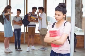 A person looking sad, standing apart from a group of teasing students.