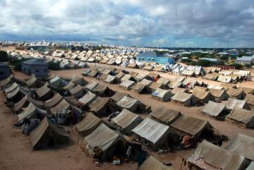Rows of tents in a large refugee camp under a cloudy sky.