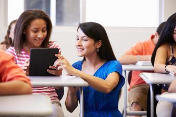 Two people studying together using a tablet in a classroom. 