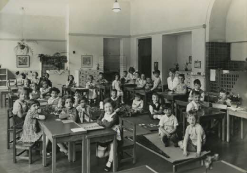 A vintage classroom with students sitting at desks and tables.