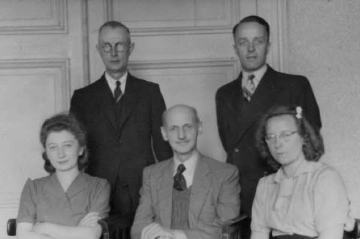 A black-and-white photograph of five people posing indoors.