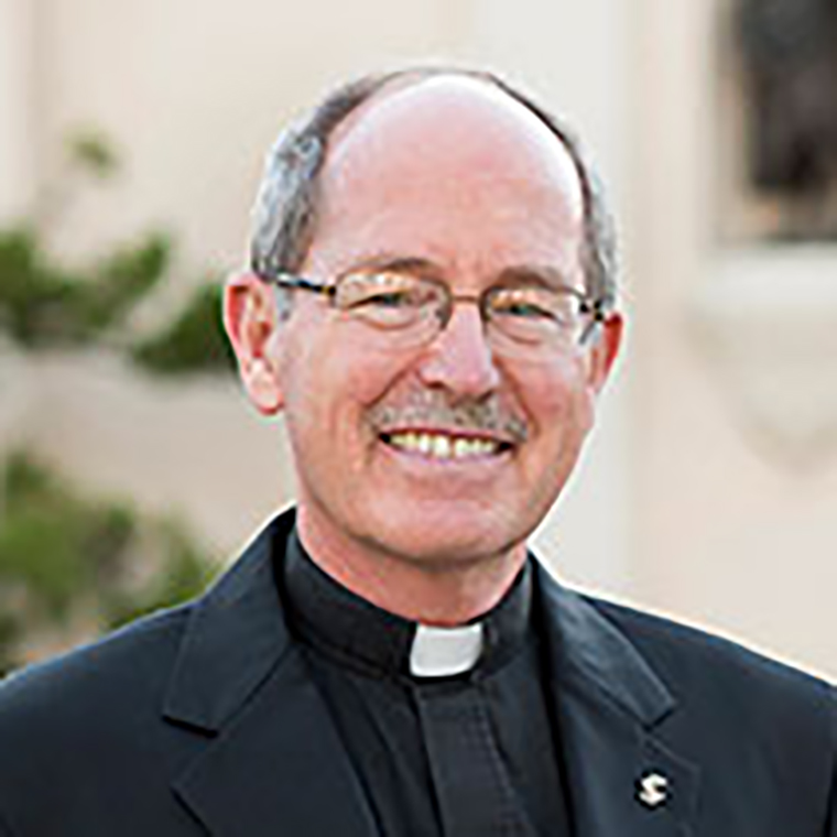 A priest smiling, wearing glasses and a black clerical shirt with a Roman collar.