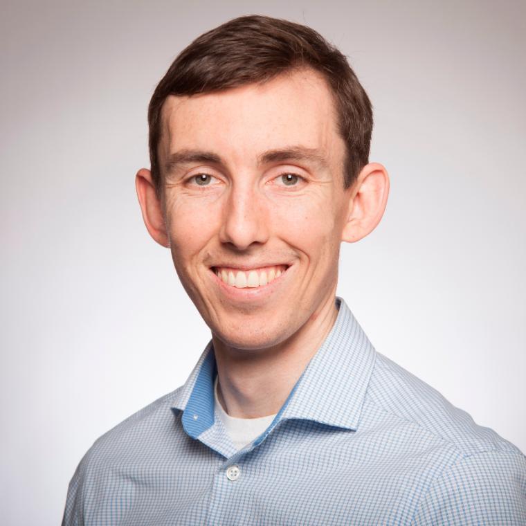 A person in a light blue collared shirt smiling.