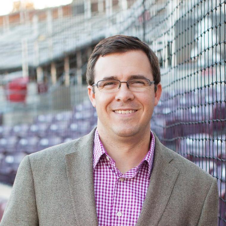 Jeff Miller smiling with the SCU baseball stands behind him