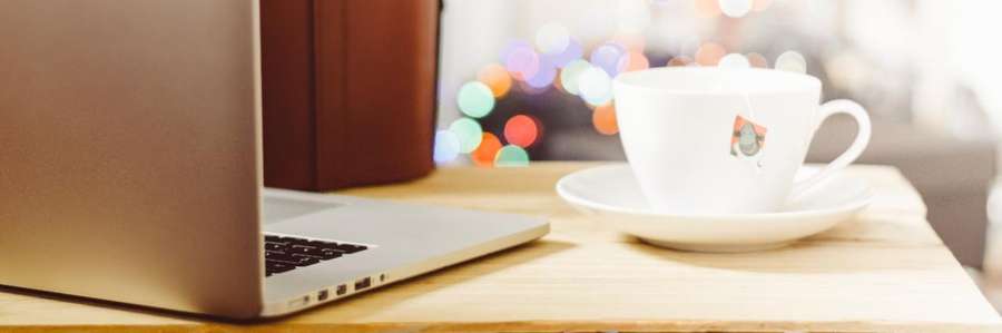 A woman typing on a laptop next to a coffee cup.
