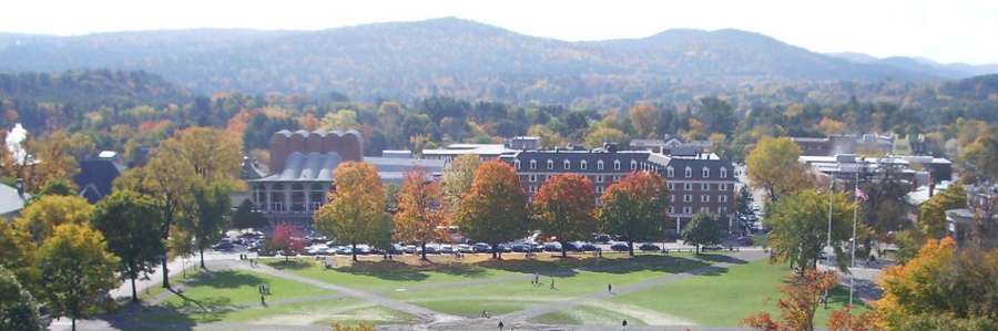 University campus with buildings, greenery, and mountains in the background on an overcast day.