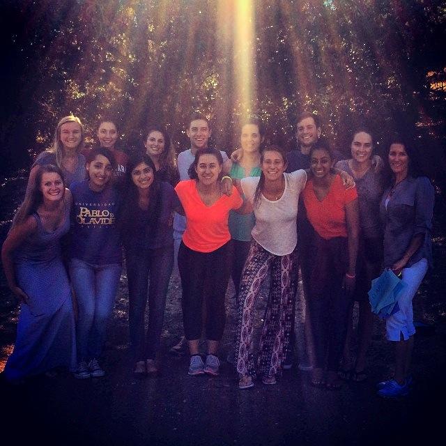 A group of people posing outside with sunlight beams above.