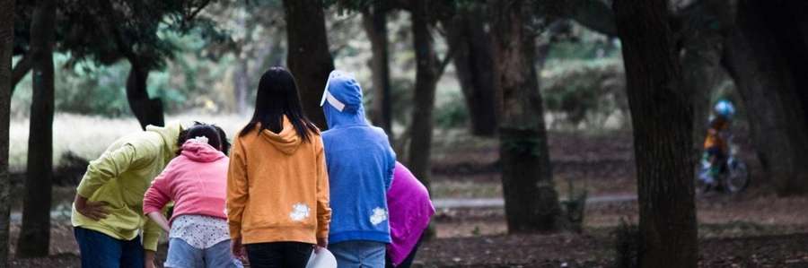 Two children walking outdoors carrying backpacks and bags.