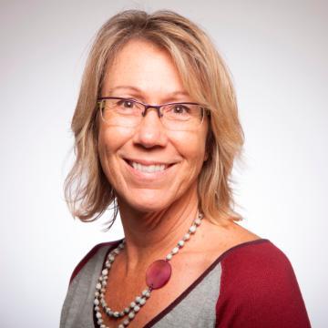 A woman wearing glasses and a necklace, smiling.