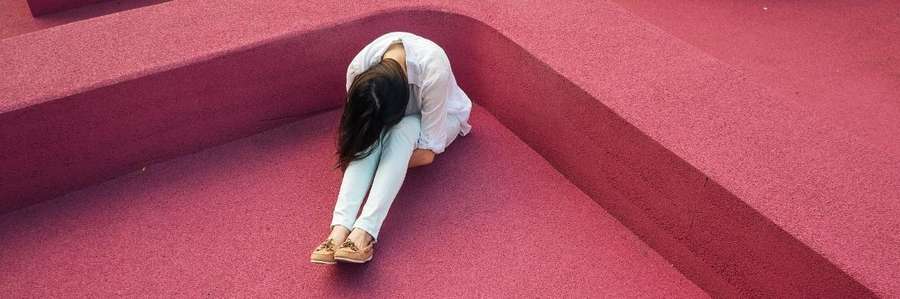 Person in white outfit and hat resting against red geometric walls.