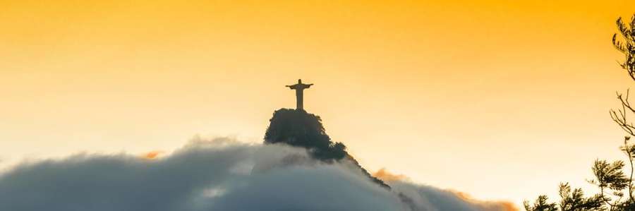 A silhouetted figure stands on a mountain at sunset.