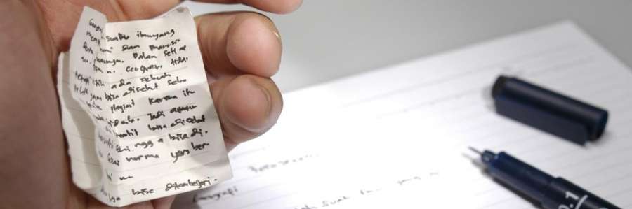A hand holding a crumpled note with handwritten text.