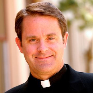 A man in clerical attire smiles at the camera.