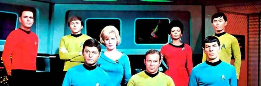 Cast of Star Trek in colorful uniforms on the bridge set.