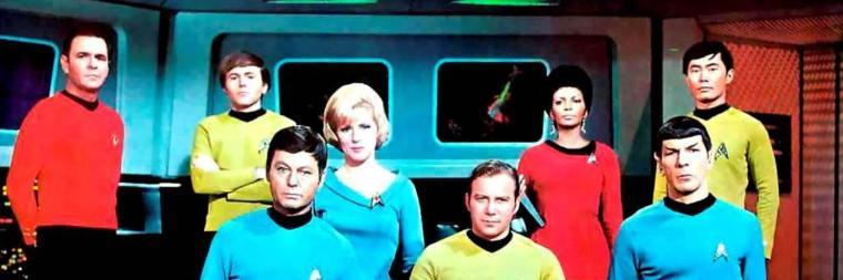 Cast of Star Trek in colorful uniforms on the bridge set.