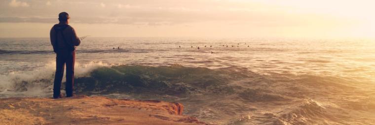 Person standing on a beach at sunset, gazing at the ocean.
