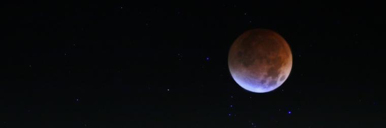 A reddish moon is prominently visible against a dark night sky.