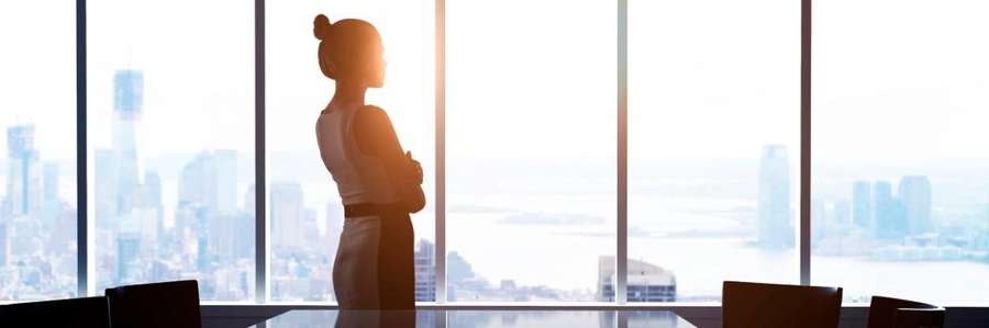 A person gazing out of floor-to-ceiling windows in a modern office setting.