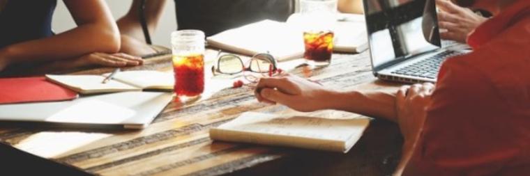 People working at a table with documents, notebooks, and drinks.