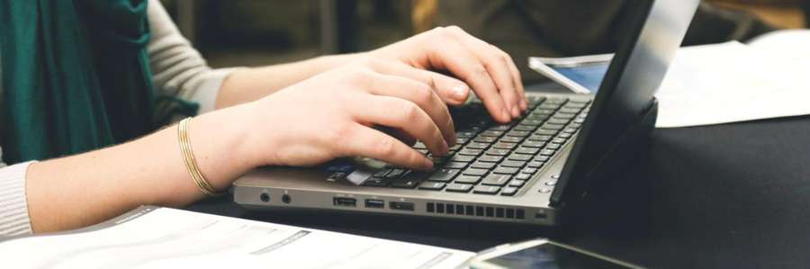Woman typing on laptop with phone next to her on desk