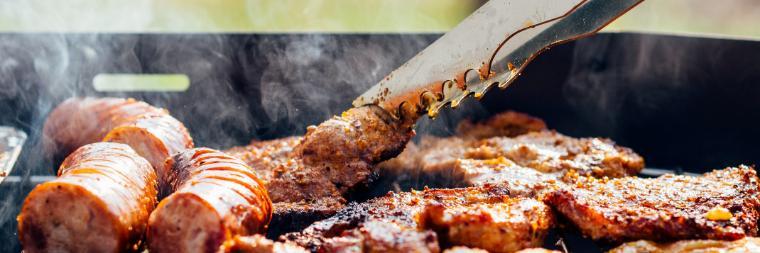 A pair of tongs flipping a burger on a grill full of hamburgers and hot dogs