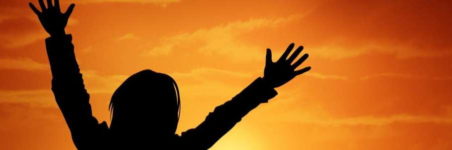 A silhouetted person with arms raised against an orange sunset.