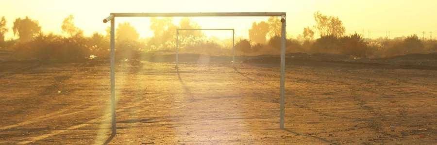 A goalpost on a misty soccer field at sunrise.